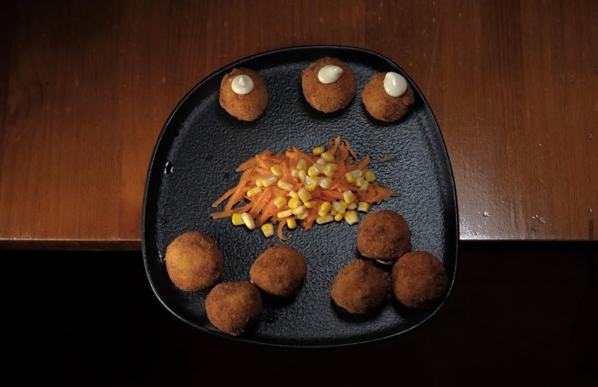 Plato negro con una variedad de aperitivos fritos y guarnición picada sobre una mesa de madera.