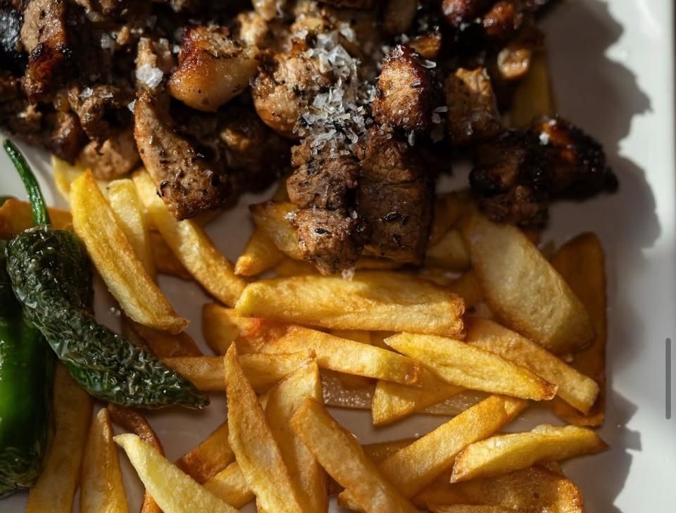 Plato de patatas fritas cubierto con carne a la parrilla sazonada y una rodaja de pimiento verde.