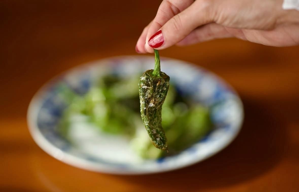 Una mano sostiene un plato con hojas verdes sobre un plato borroso en una mesa de madera.