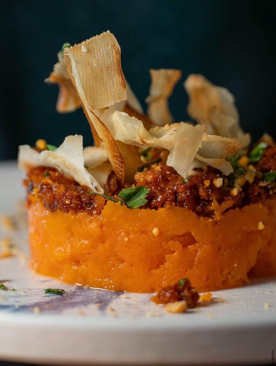 Postre de naranja cubierto con nueces desmenuzadas y finas virutas de hojaldre sobre un plato blanco.
