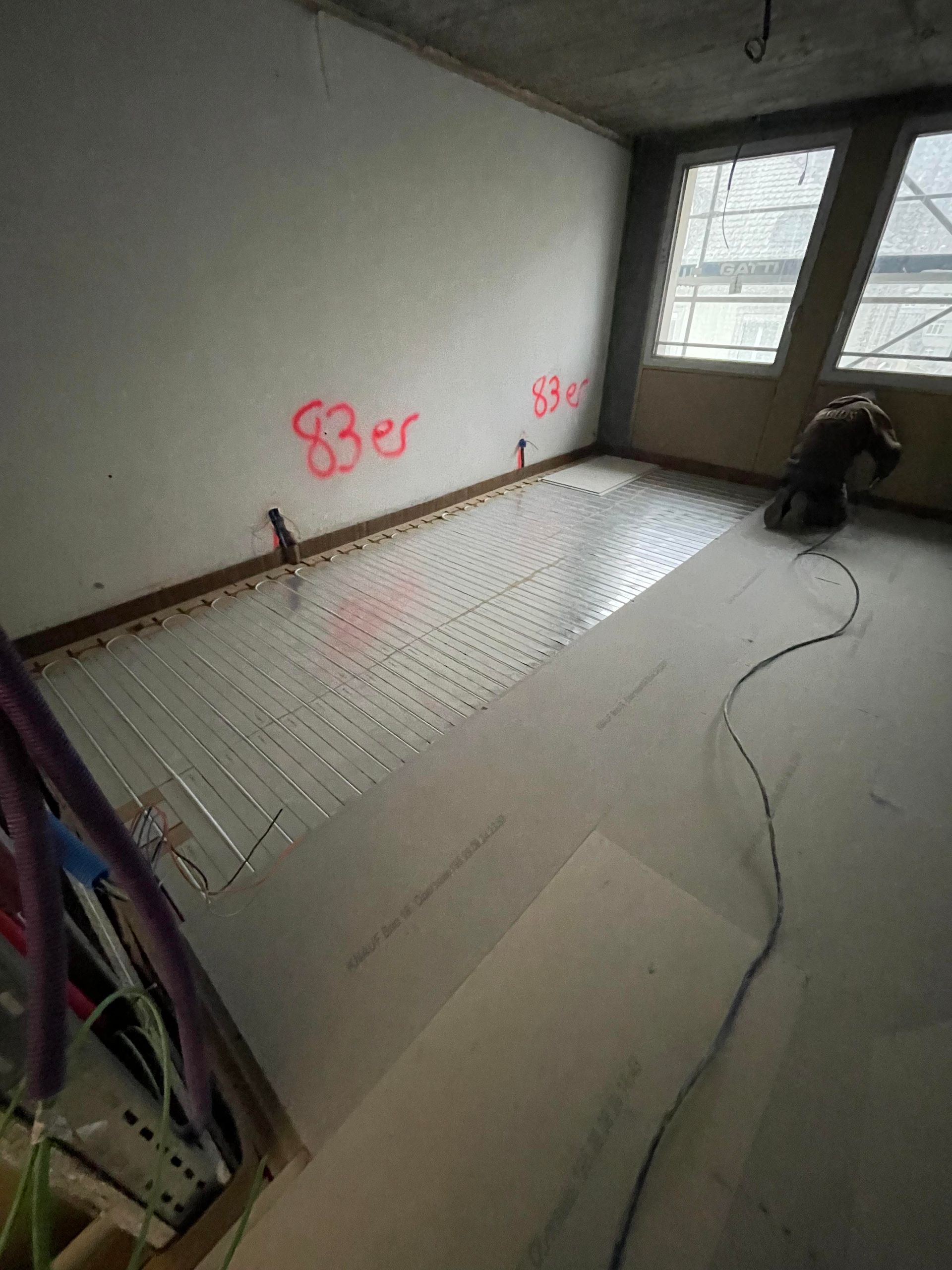 Ein Mann arbeitet an einem Fußboden in einem Raum mit vielen Fenstern.