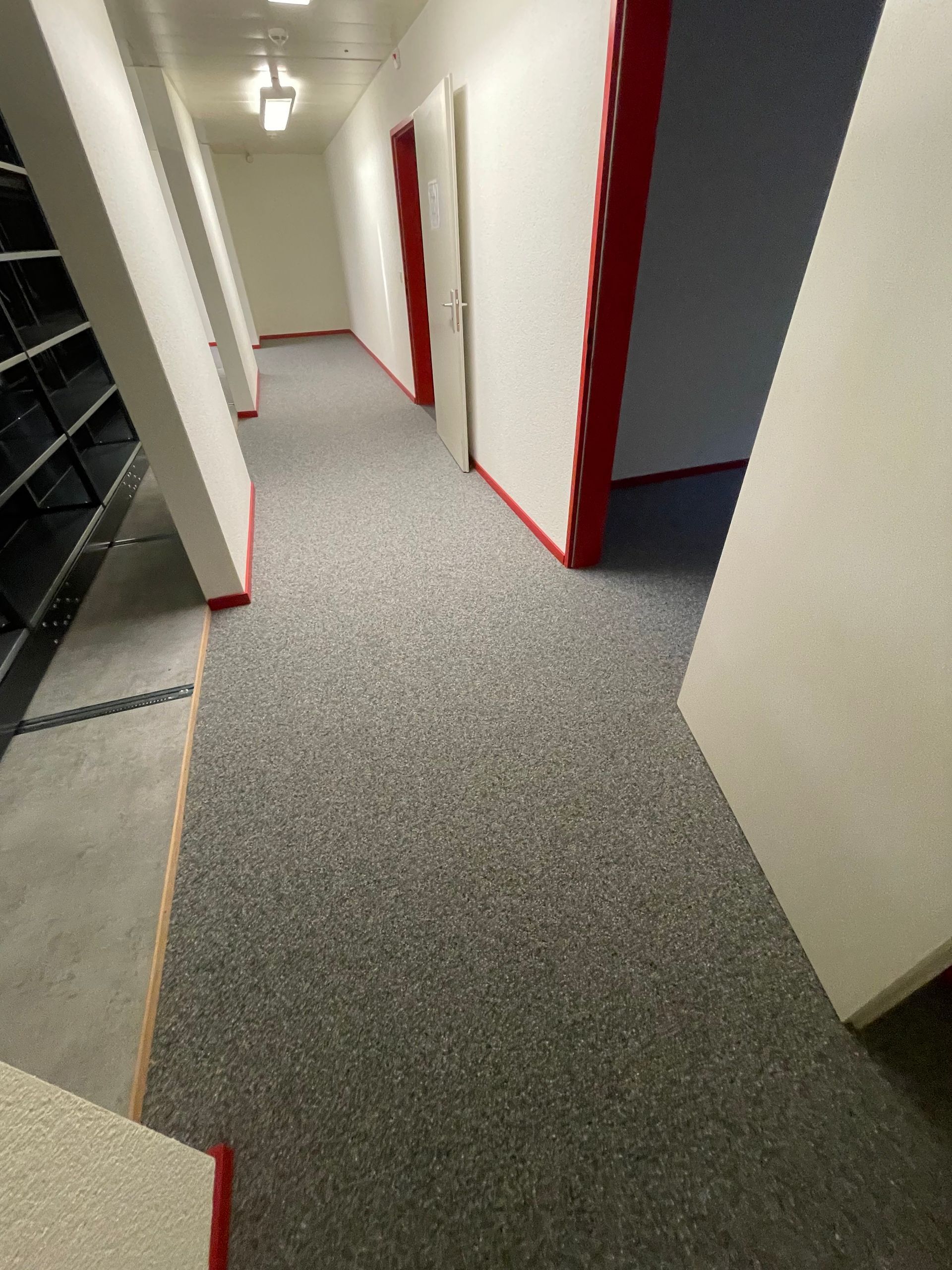 Ein langer Flur mit Teppichboden und roten Zierleisten.