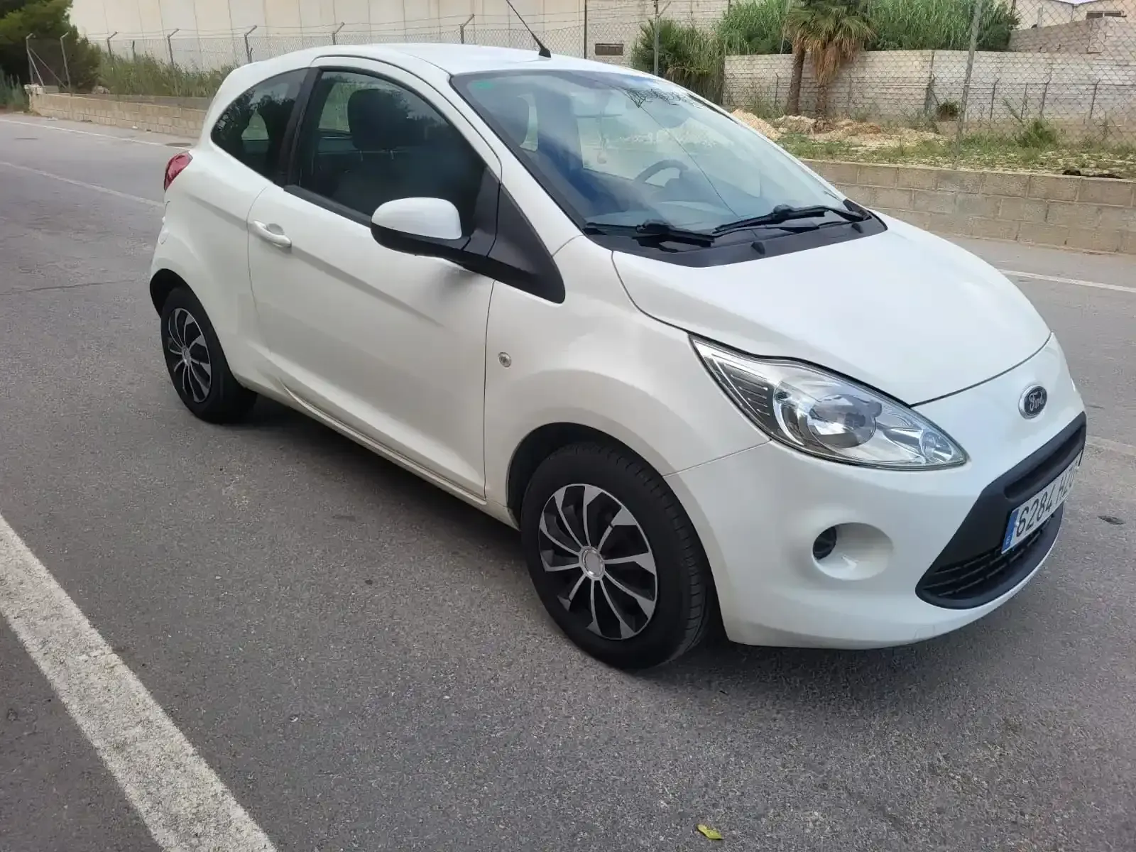 Ford Ka blanco estacionado en la carretera asfaltada.