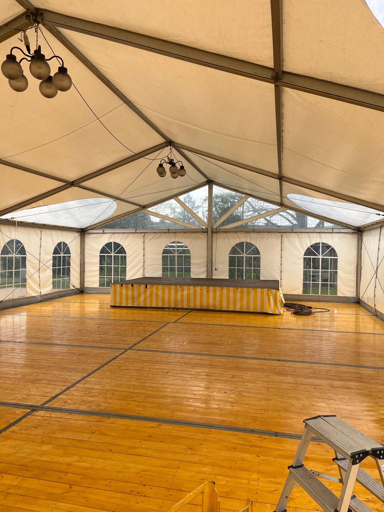 Ein großes leeres Zelt mit Holzboden und einem Kronleuchter, der von der Decke hängt.