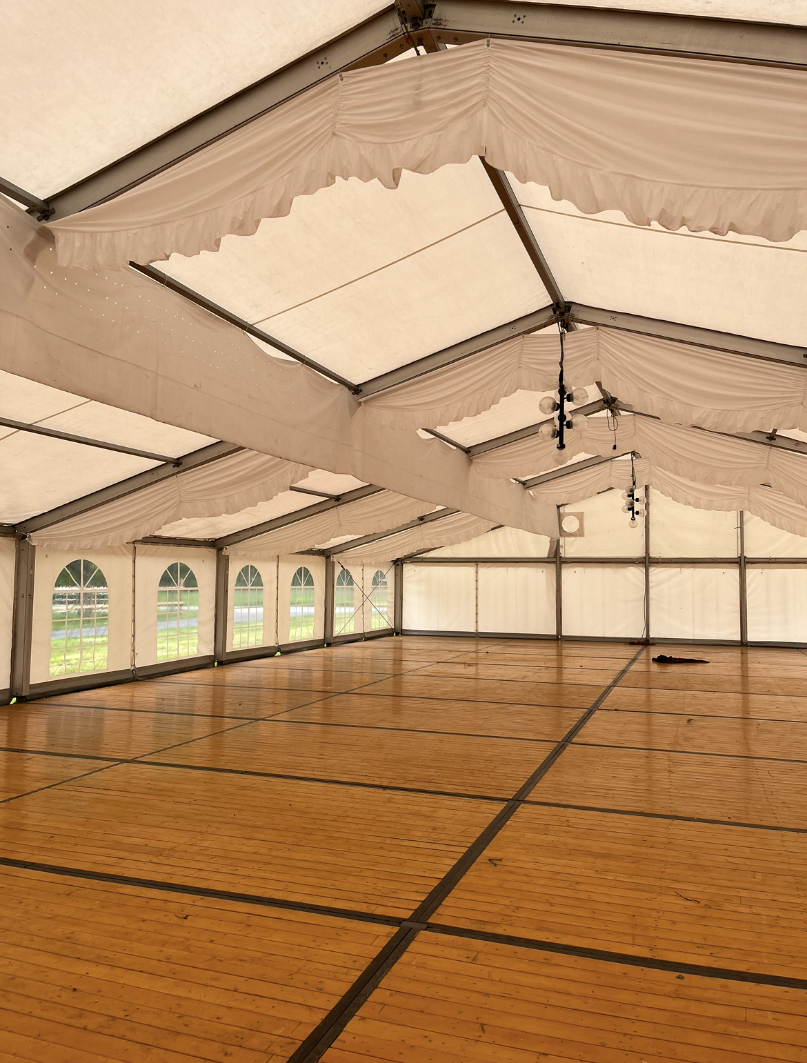 Ein großes leeres Zelt mit Holzboden und weißen Vorhängen.