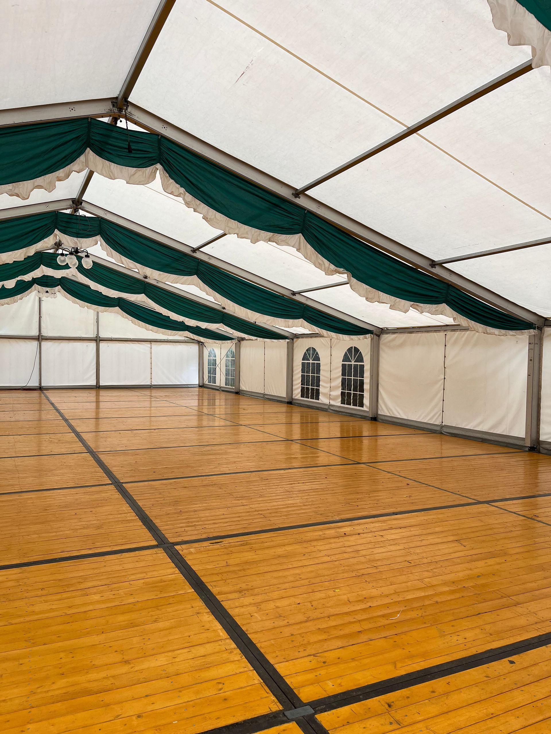 Ein großes leeres Zelt mit Holzboden und grün-weißer Decke.