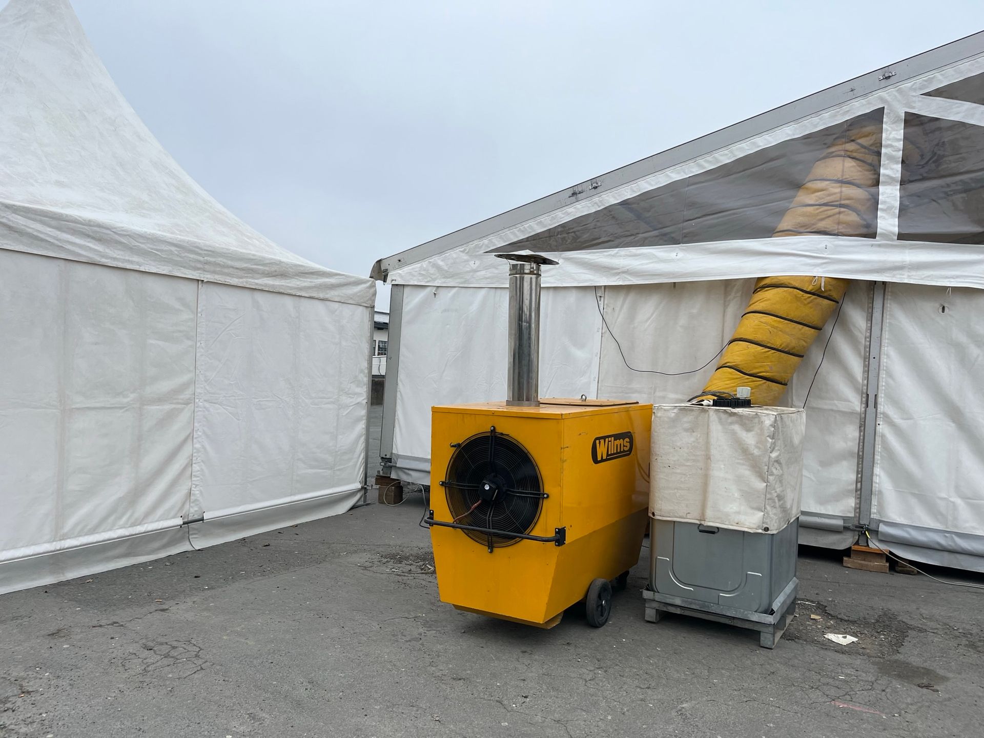 Vor einem weißen Zelt steht ein gelber Heizstrahler.