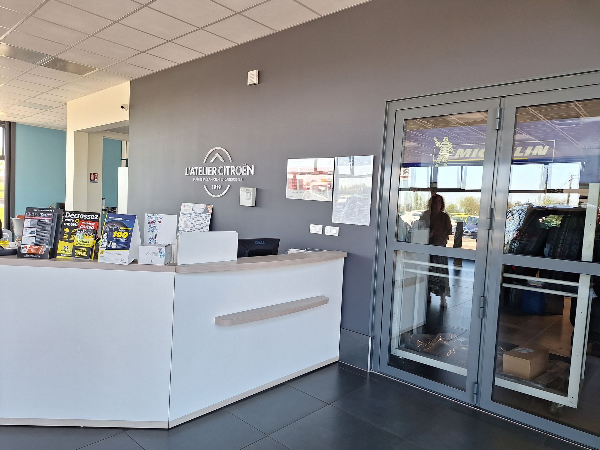 Zone d'accueil du garage avec comptoir blanc et brochures d'information