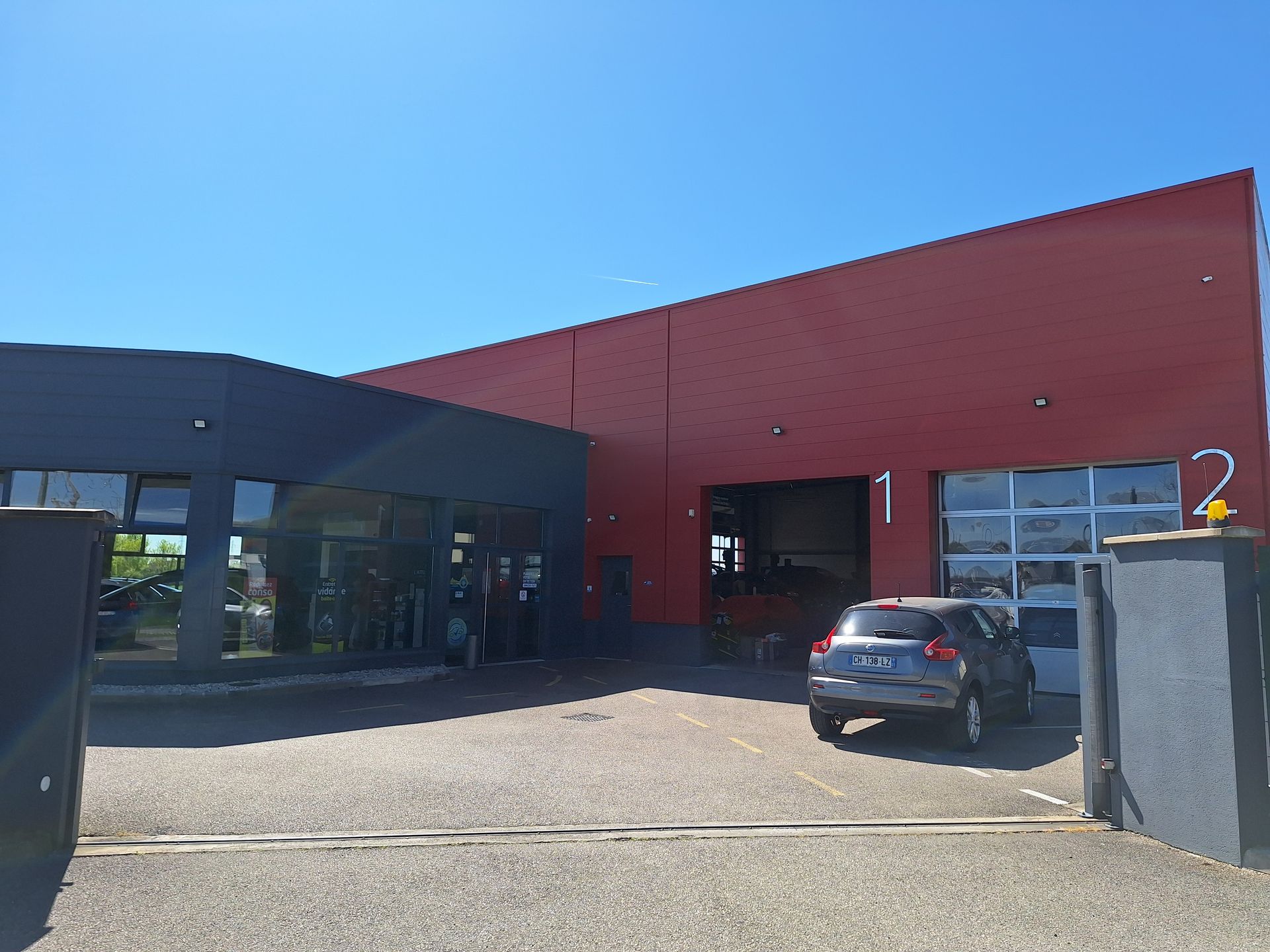 Entrée du garage automobile avec bâtiment rouge et véhicules stationnés