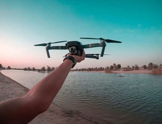 Una persona sostiene un dron sobre un cuerpo de agua.