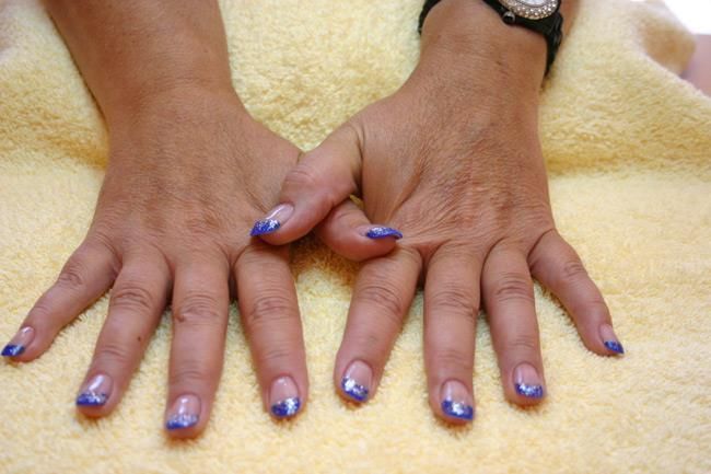 Die Hände einer Frau mit blauen Nägeln und einer Uhr auf einem gelben Handtuch.