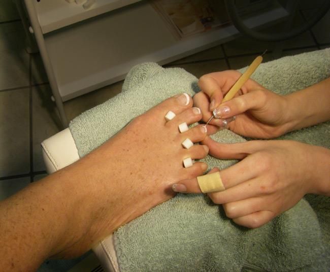 Eine Frau lackiert einem Mann mit einem Pinsel die Fußnägel