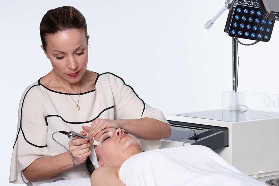 Eine Frau bearbeitet mit einer Maschine das Gesicht einer Frau.