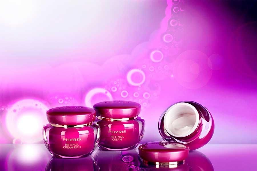 Drei rosafarbene Tiegel mit Kosmetika stehen auf einer violetten Fläche.