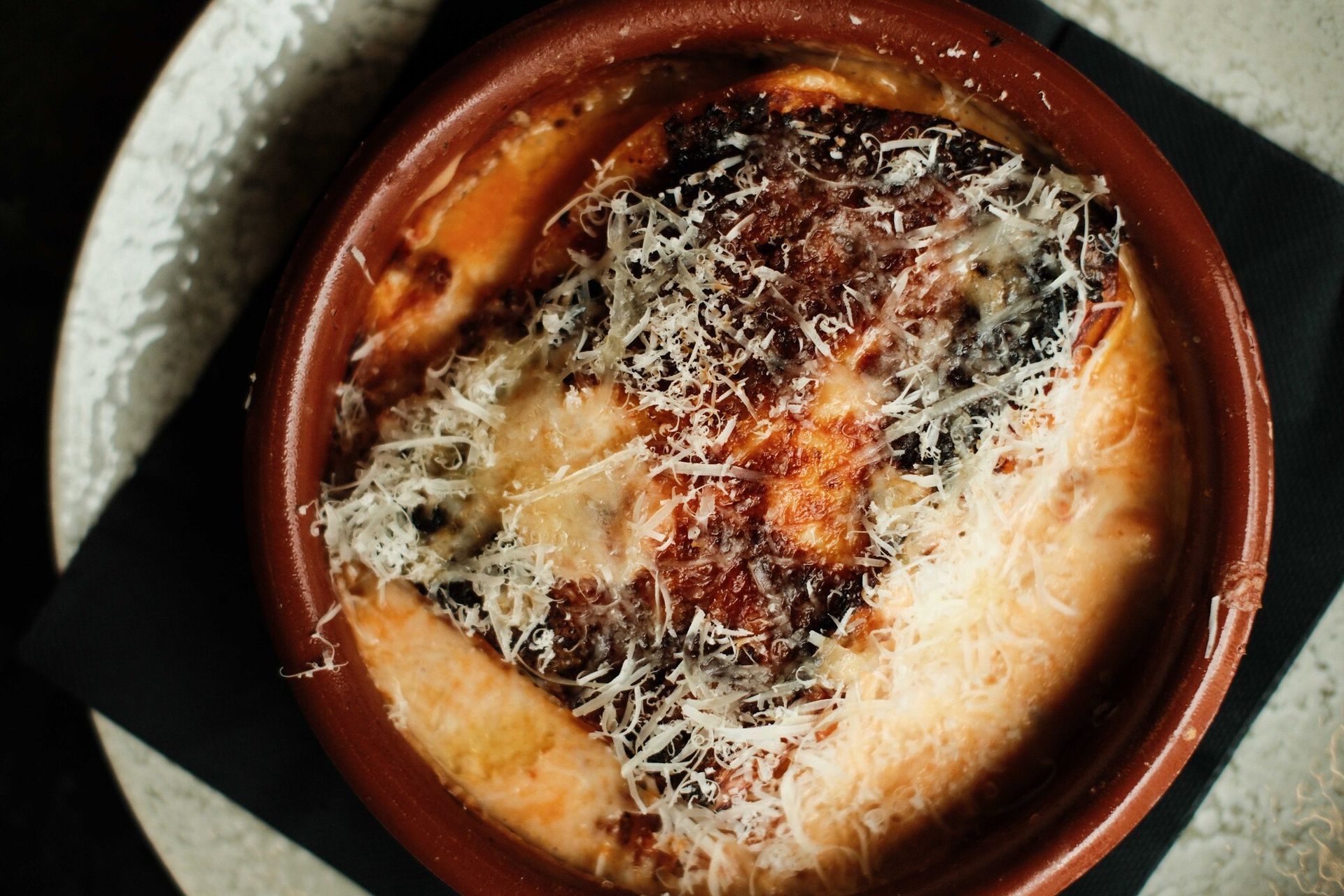 Plato horneado con queso derretido en recipiente de barro marrón.