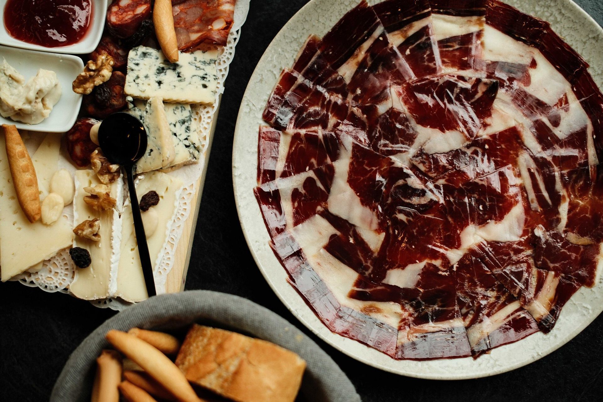 Tabla de embutidos con fiambres, quesos y mermelada; pan y palitos de pan.