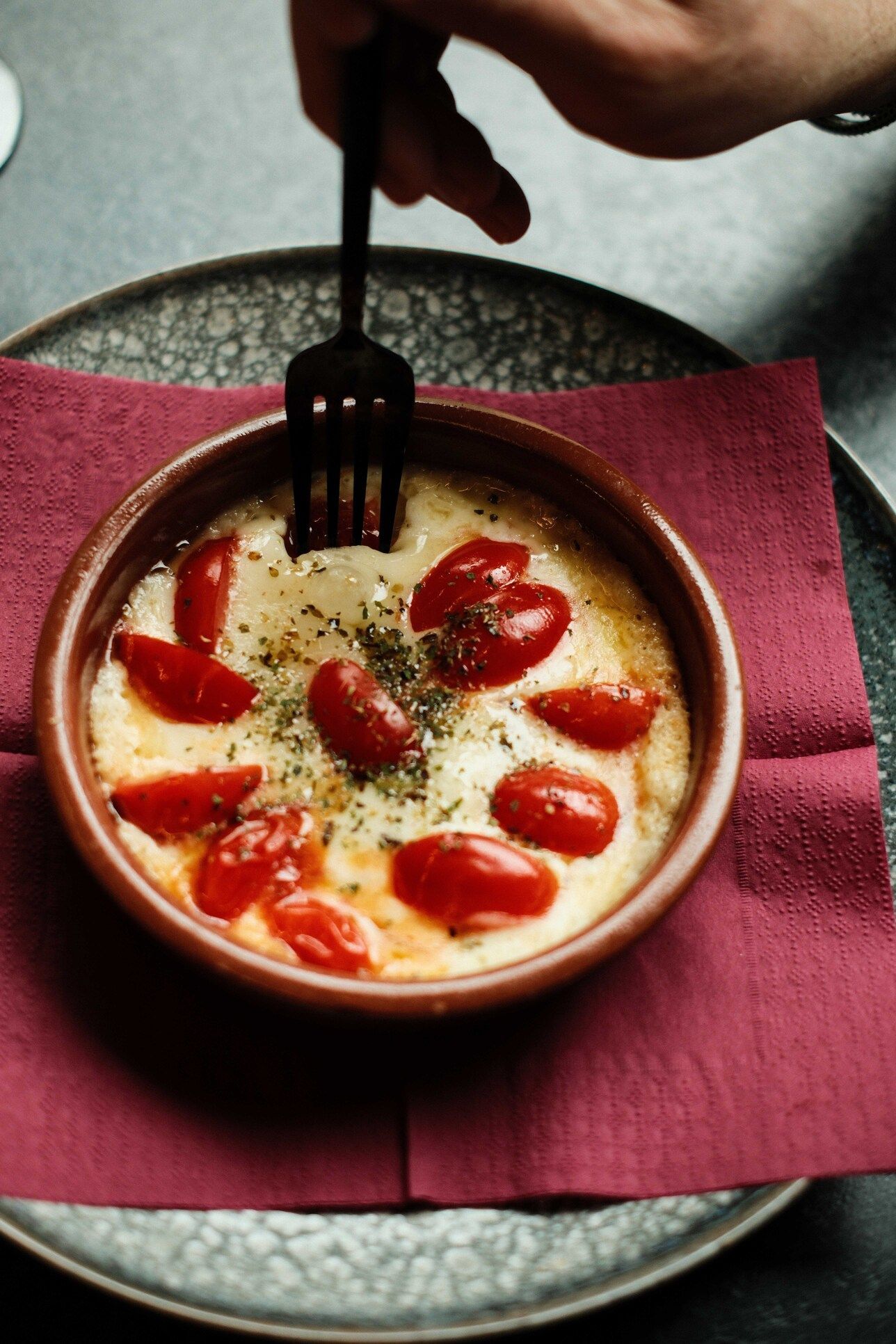 Plato de queso al horno con tomates, pinchados con un tenedor, sobre una servilleta y un plato de color rojo.