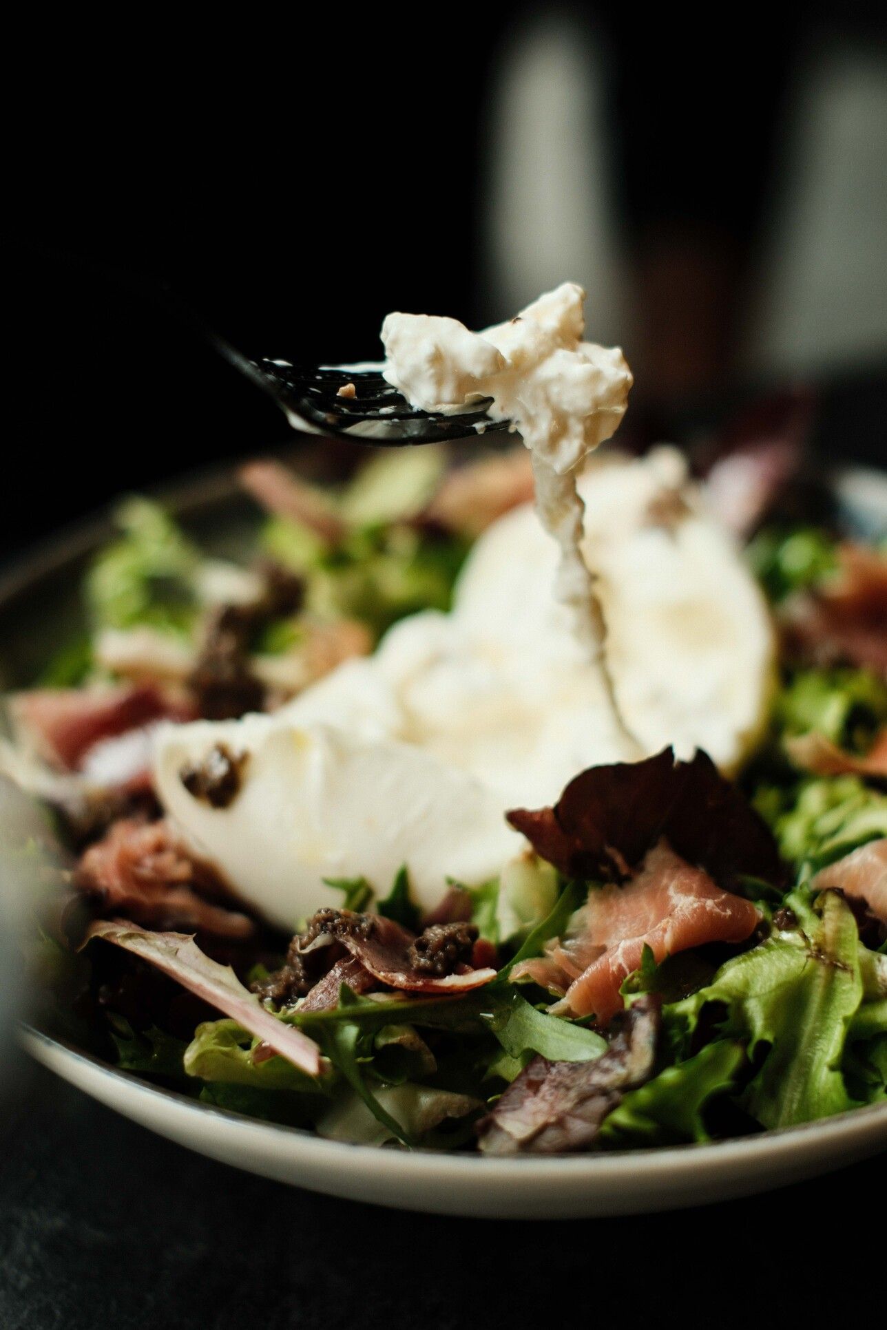 Ensalada de burrata con prosciutto y verduras; queso al tenedor.