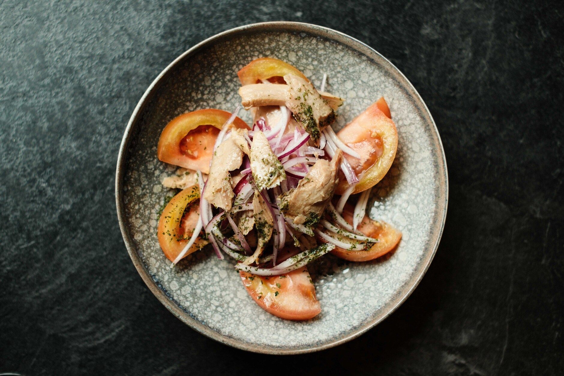 Ensalada de tomate y atún con cebolla roja en un plato gris.