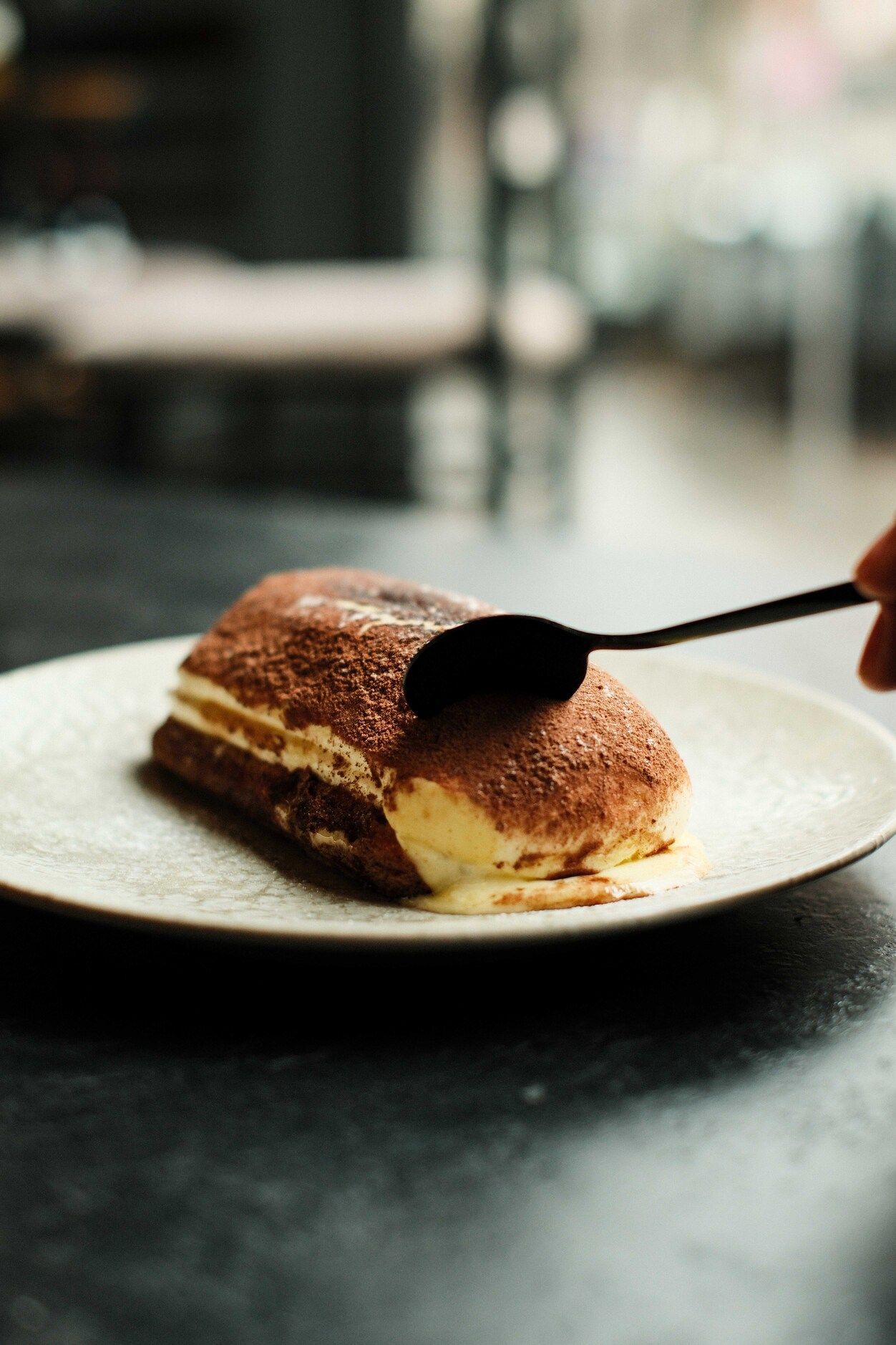 Tiramisú en un plato blanco; una cuchara negra sirve para servir un bocado.