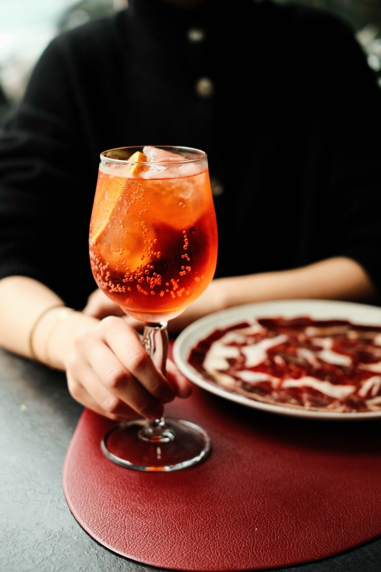 Persona sosteniendo un cóctel con burbujas y un plato de comida.