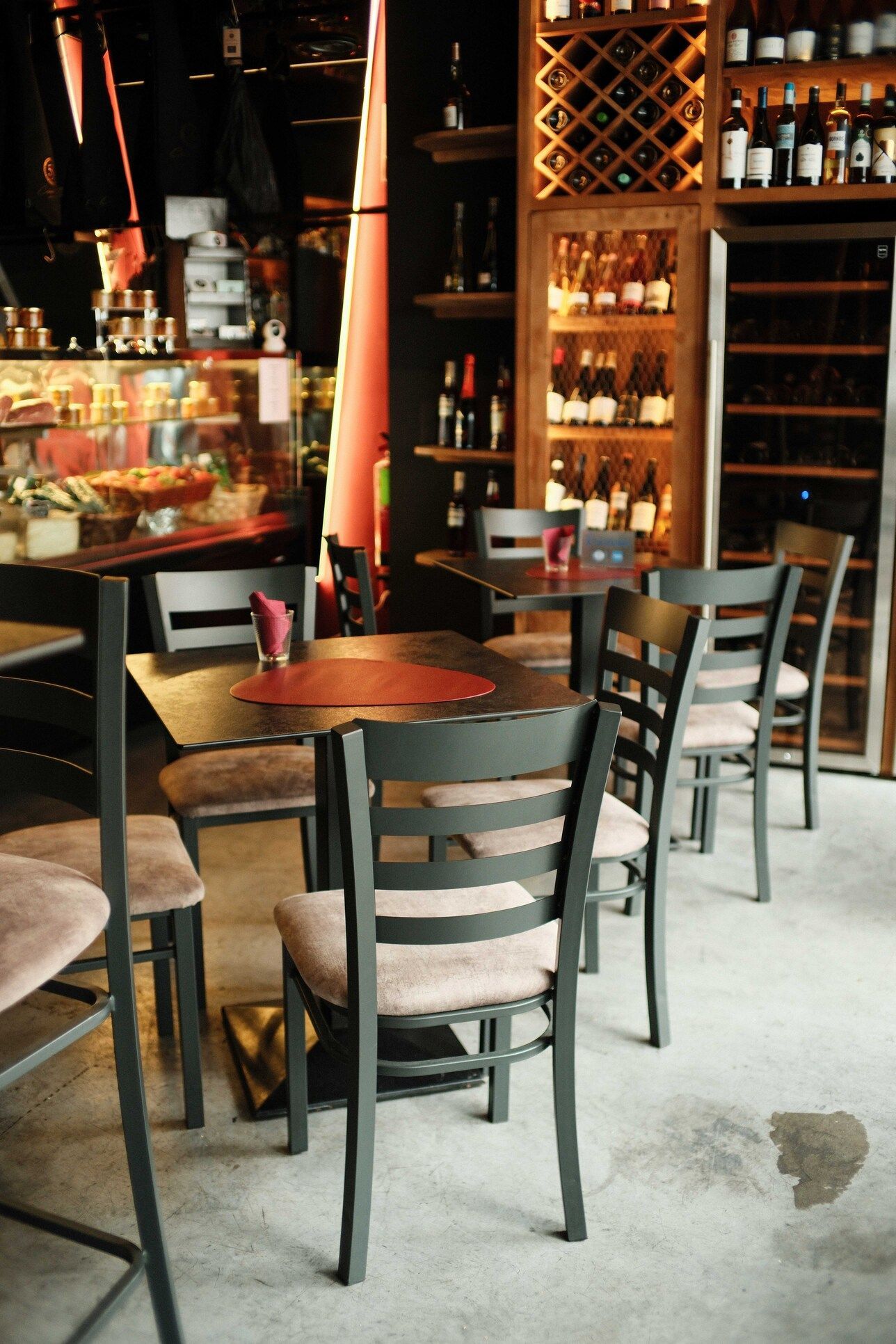 Interior de un restaurante con mesas y sillas de madera, botelleros y vitrina de comida.