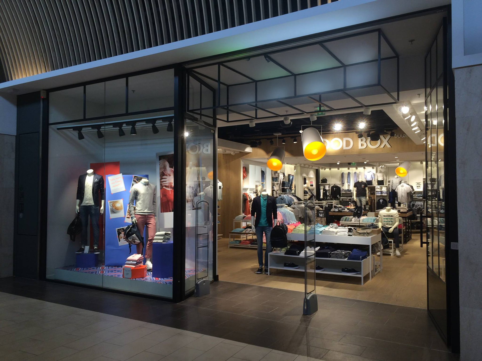 Vitrine avec portes vitrées ; vêtements exposés à l’intérieur. Éclairage intérieur par spots et suspensions.