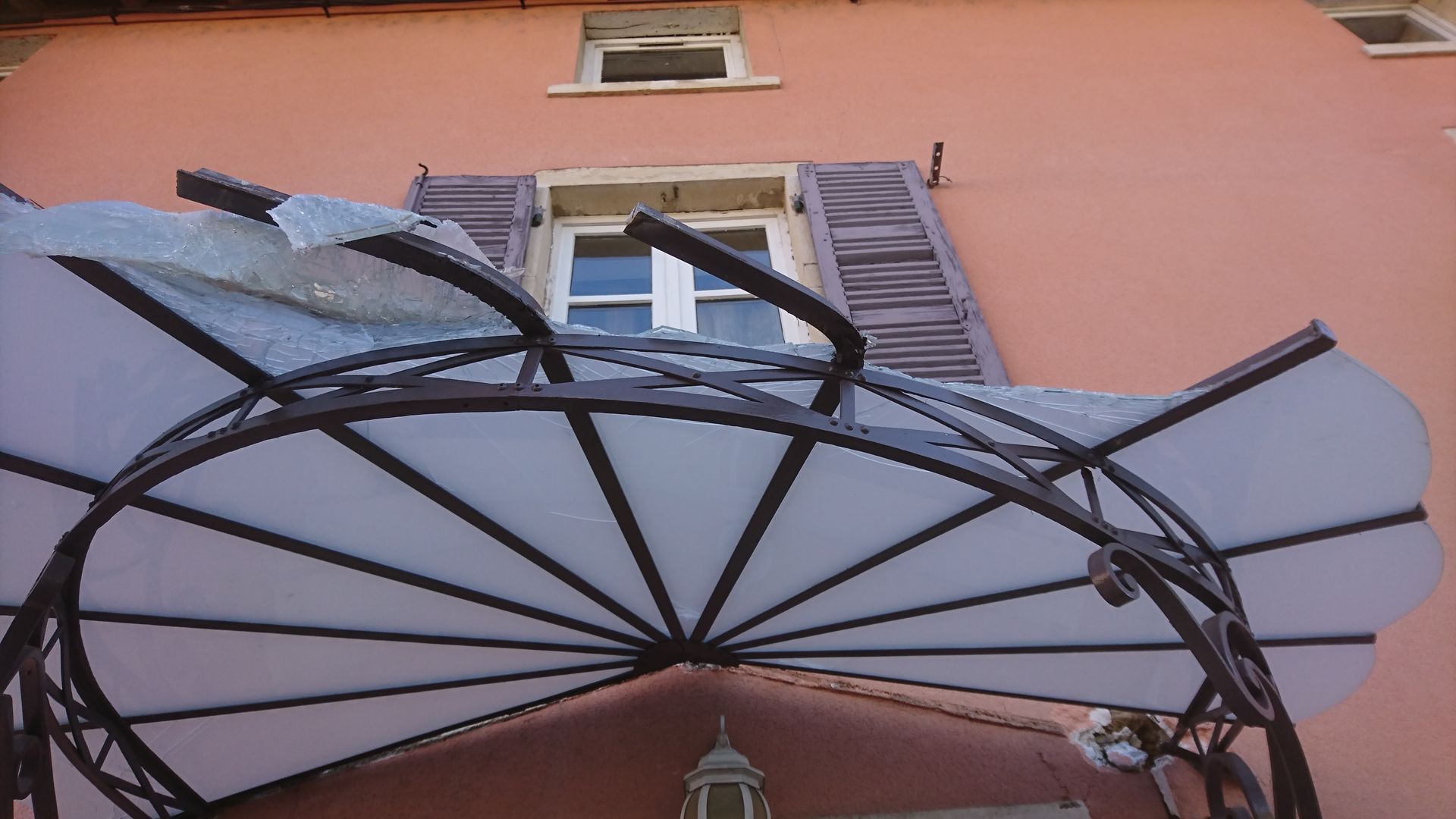 Un auvent décoratif en fer forgé à panneaux blancs surplombe une porte sur la façade claire d'un bâtiment.