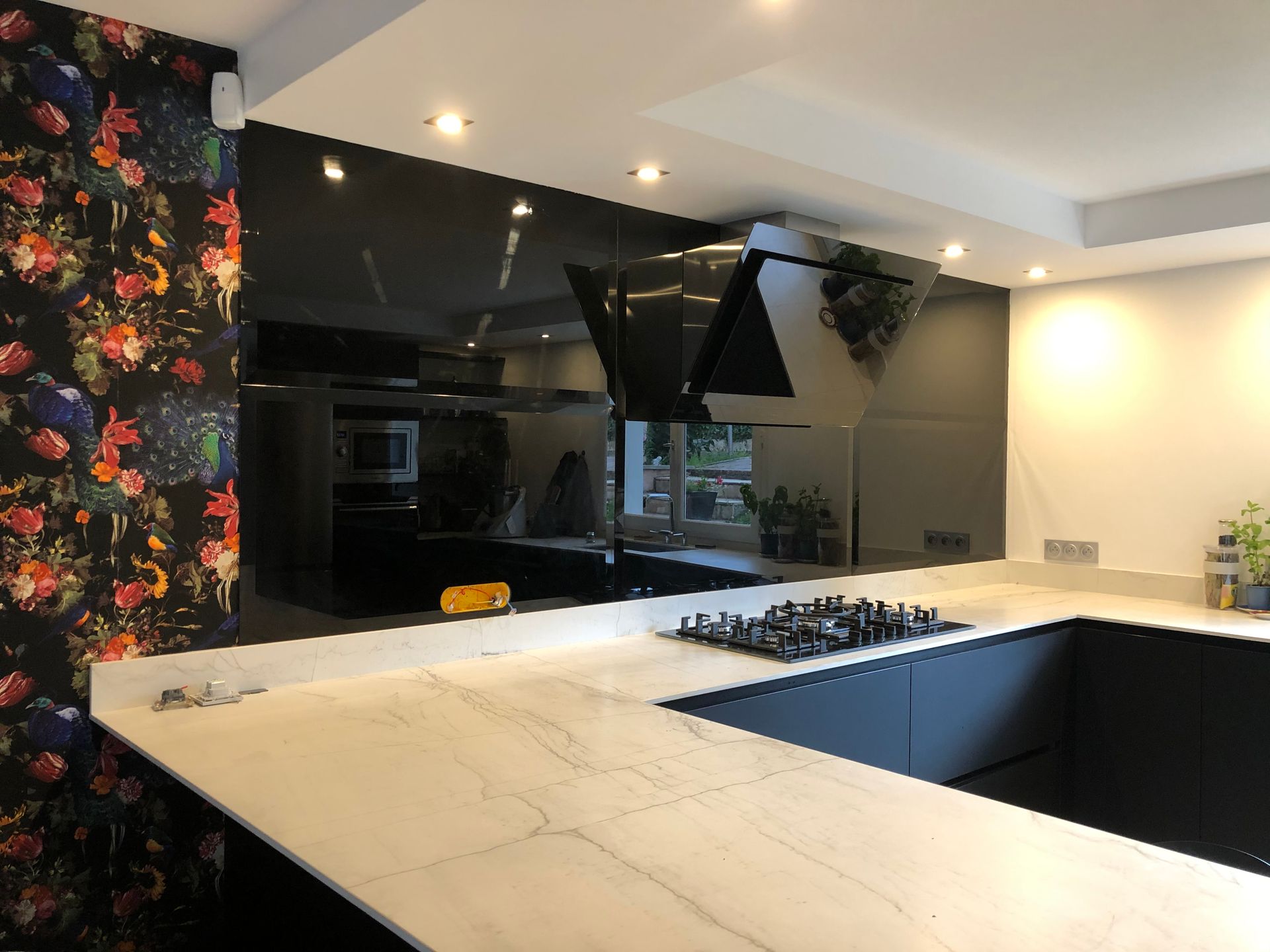 Une cuisine moderne avec un plan de travail en marbre blanc, des meubles foncés et une crédence en verre noir réfléchissant.