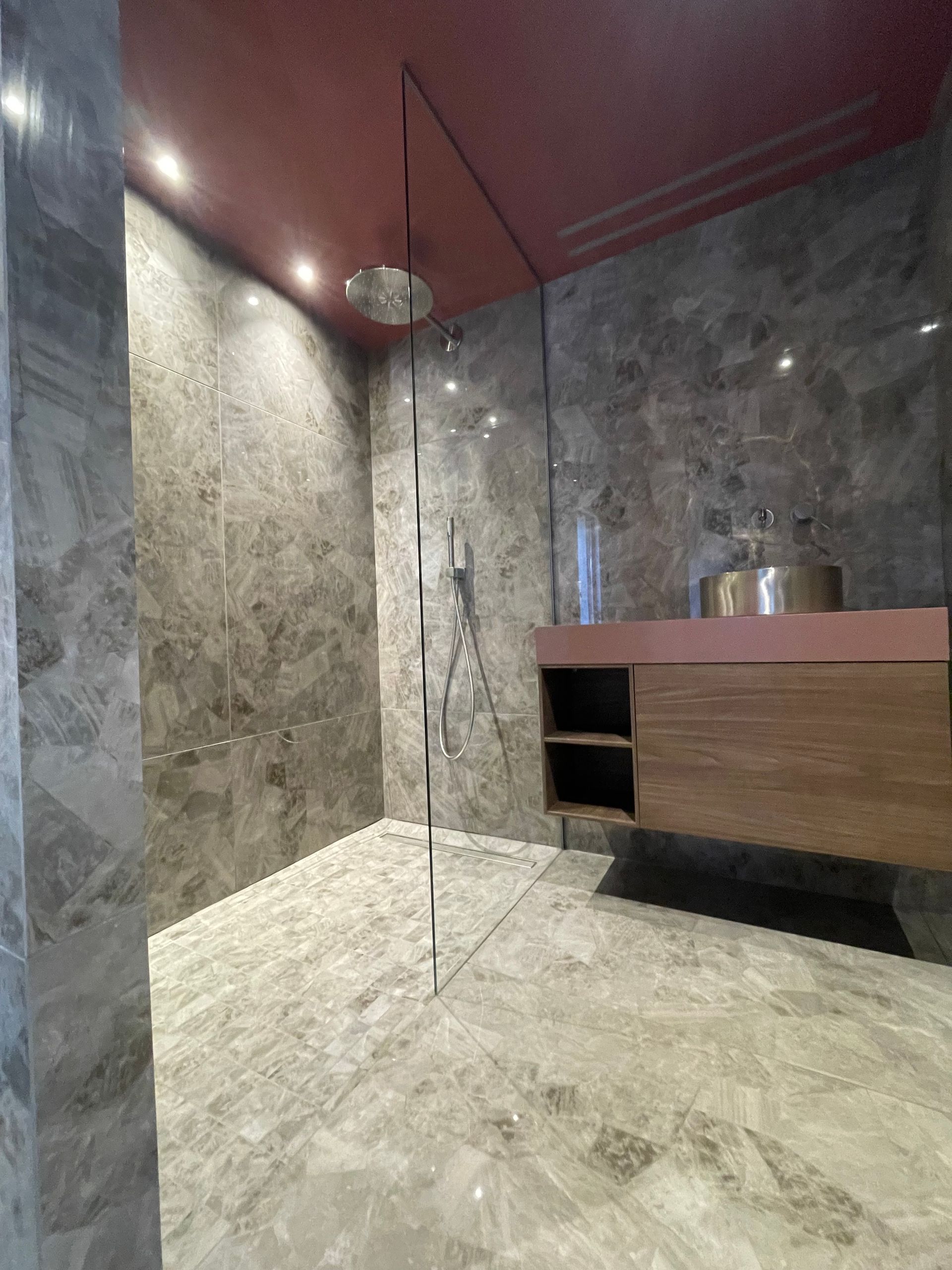 Salle de bains moderne avec murs et sol en marbre gris, paroi de douche en verre et meuble-lavabo suspendu en bois.