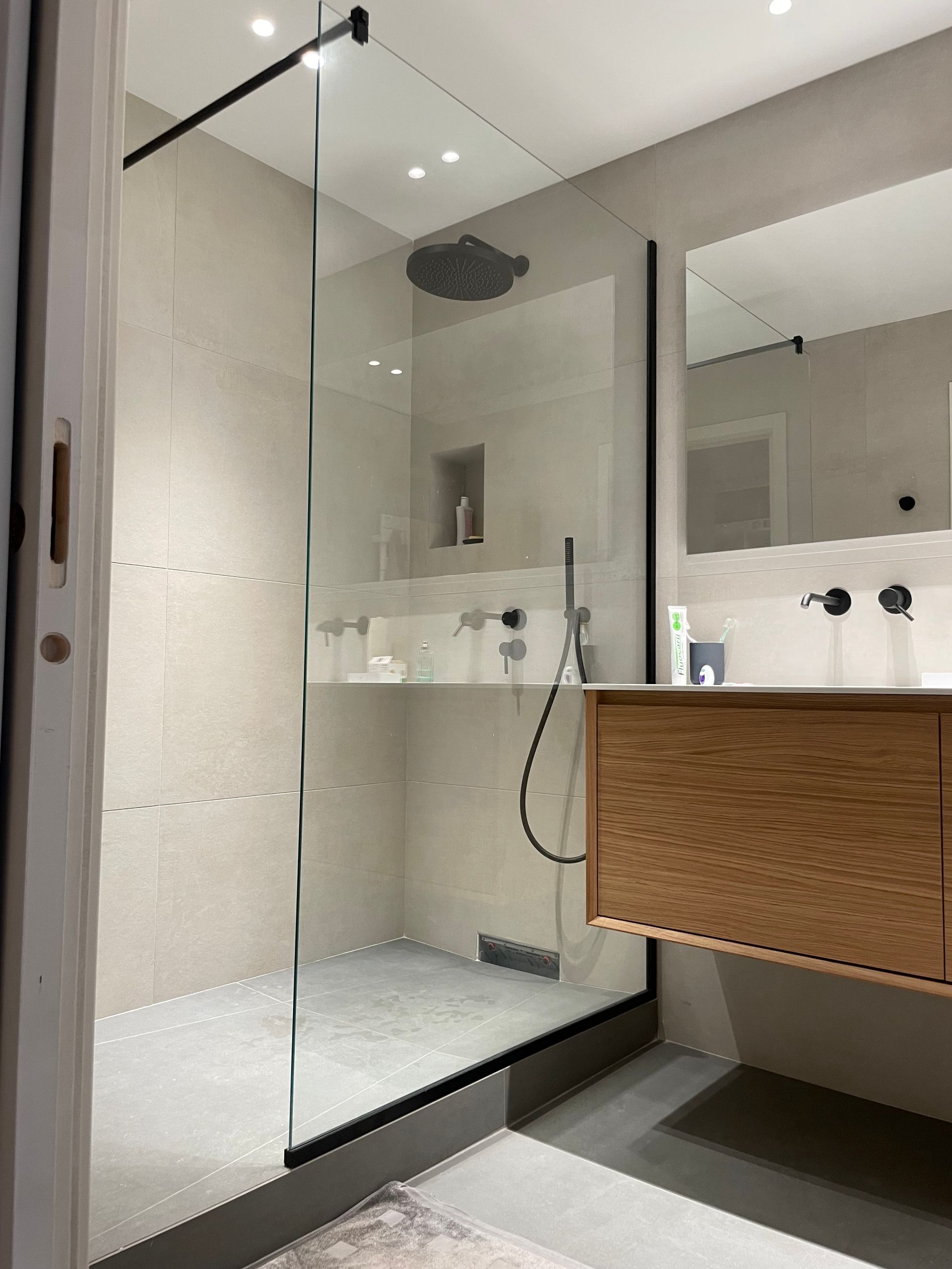 Une salle de bains moderne dotée d'une douche à l'italienne avec cadre noir, paroi en verre et meuble-lavabo suspendu en bois clair.