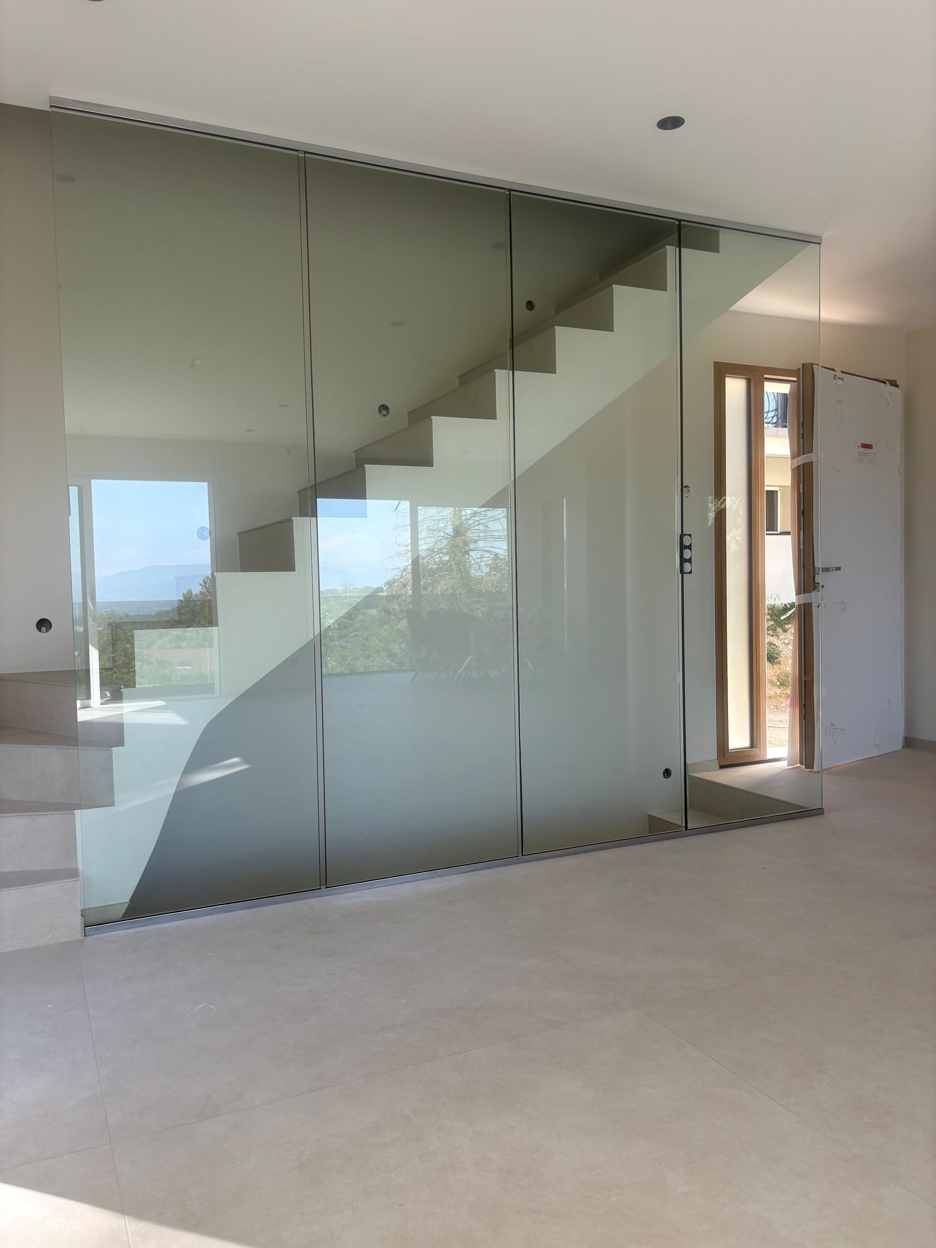Escalier en verre dans une pièce moderne inachevée avec de grandes fenêtres et un sol recouvert de moquette