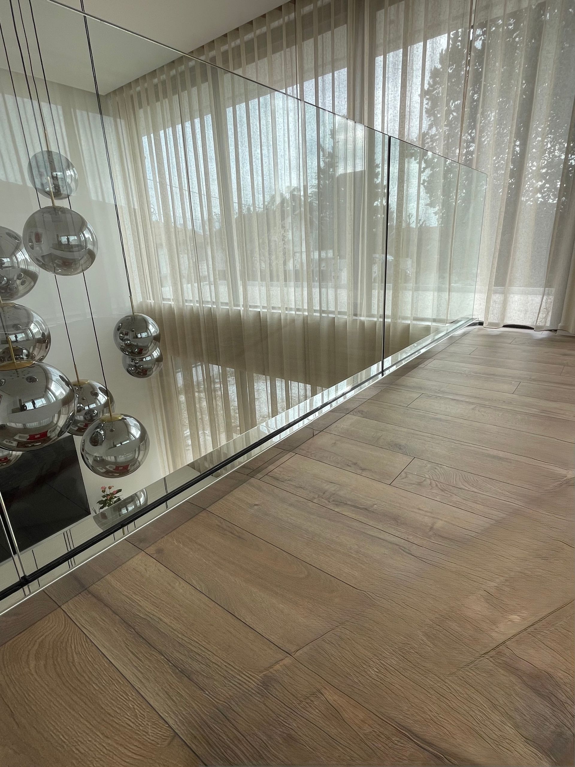 Un intérieur de loft moderne avec parquet à chevrons, une balustrade en verre transparent et un ensemble de suspensions lumineuses en forme de globe.