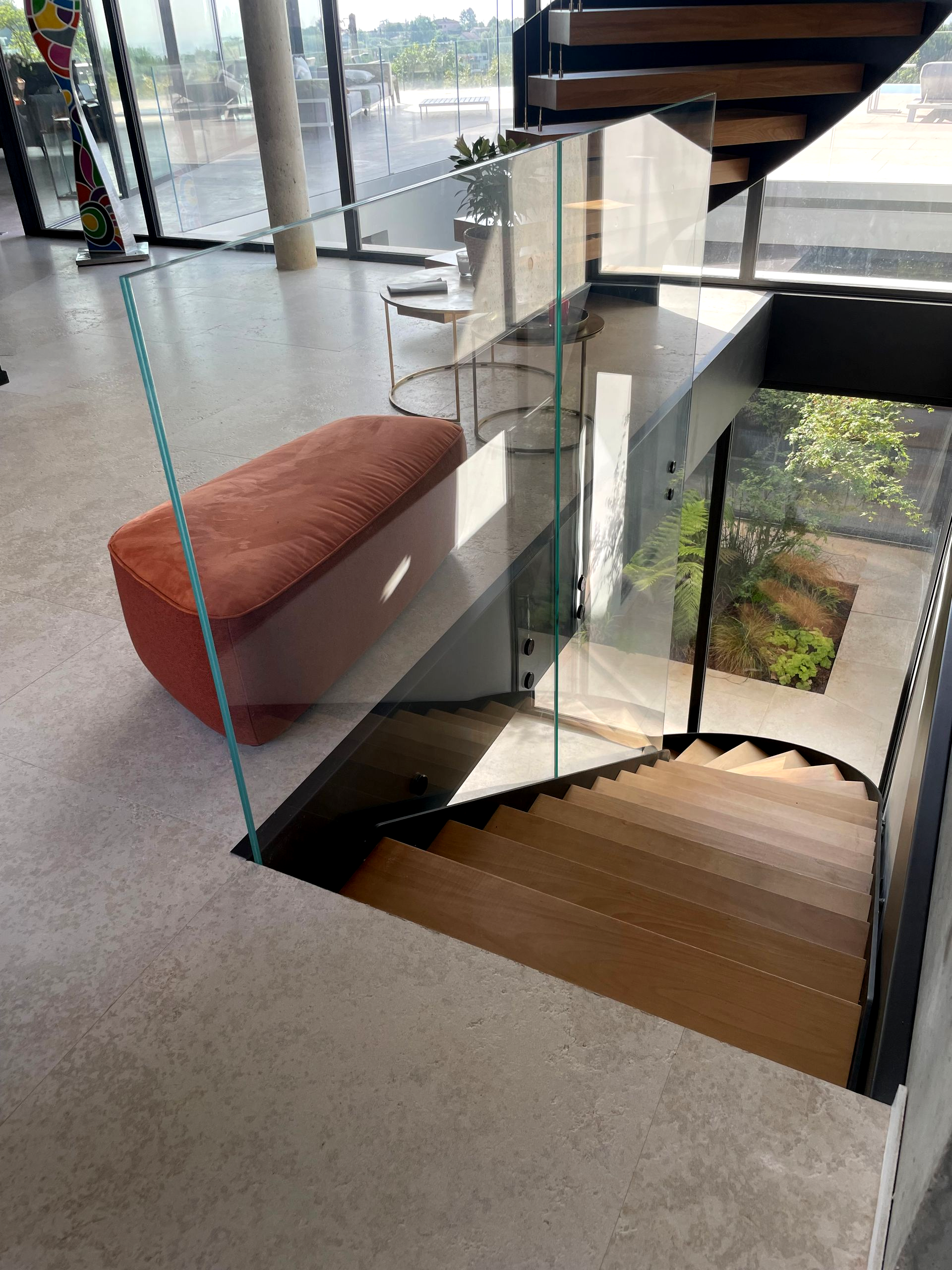 Intérieur moderne avec escalier, balustrade en verre et banc orange.