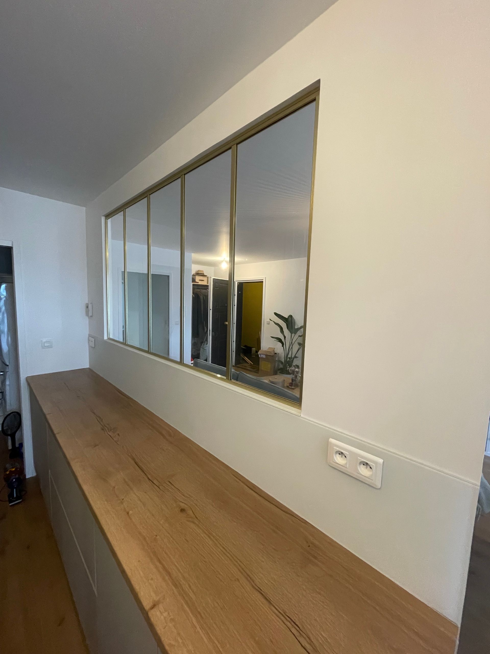 Longue armoire en bois avec une fenêtre horizontale et des miroirs, dans une pièce aux murs blancs.