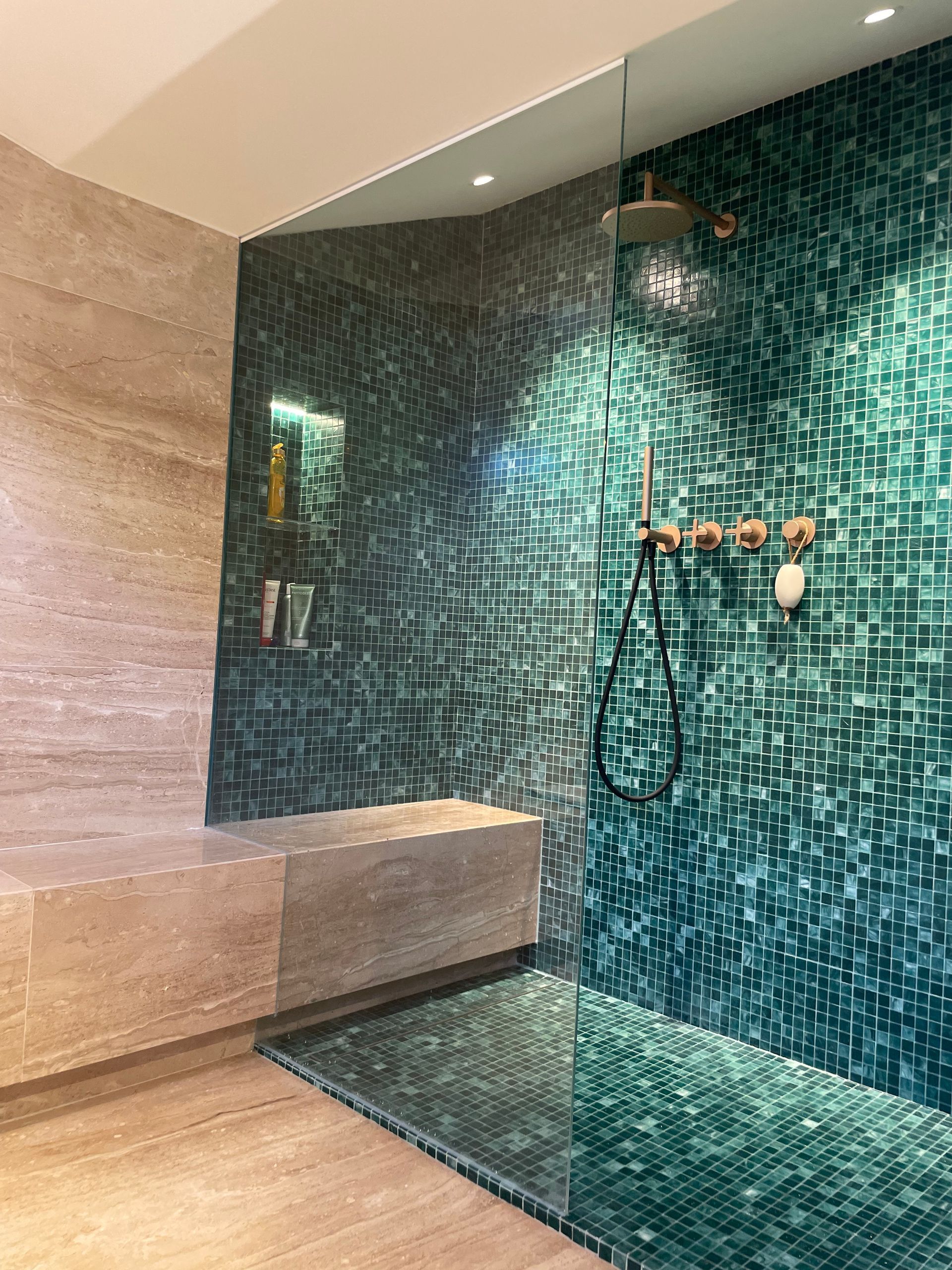 Une douche à l'italienne moderne avec des carreaux de mosaïque vert foncé, un grand banc en pierre et des panneaux muraux en verre.