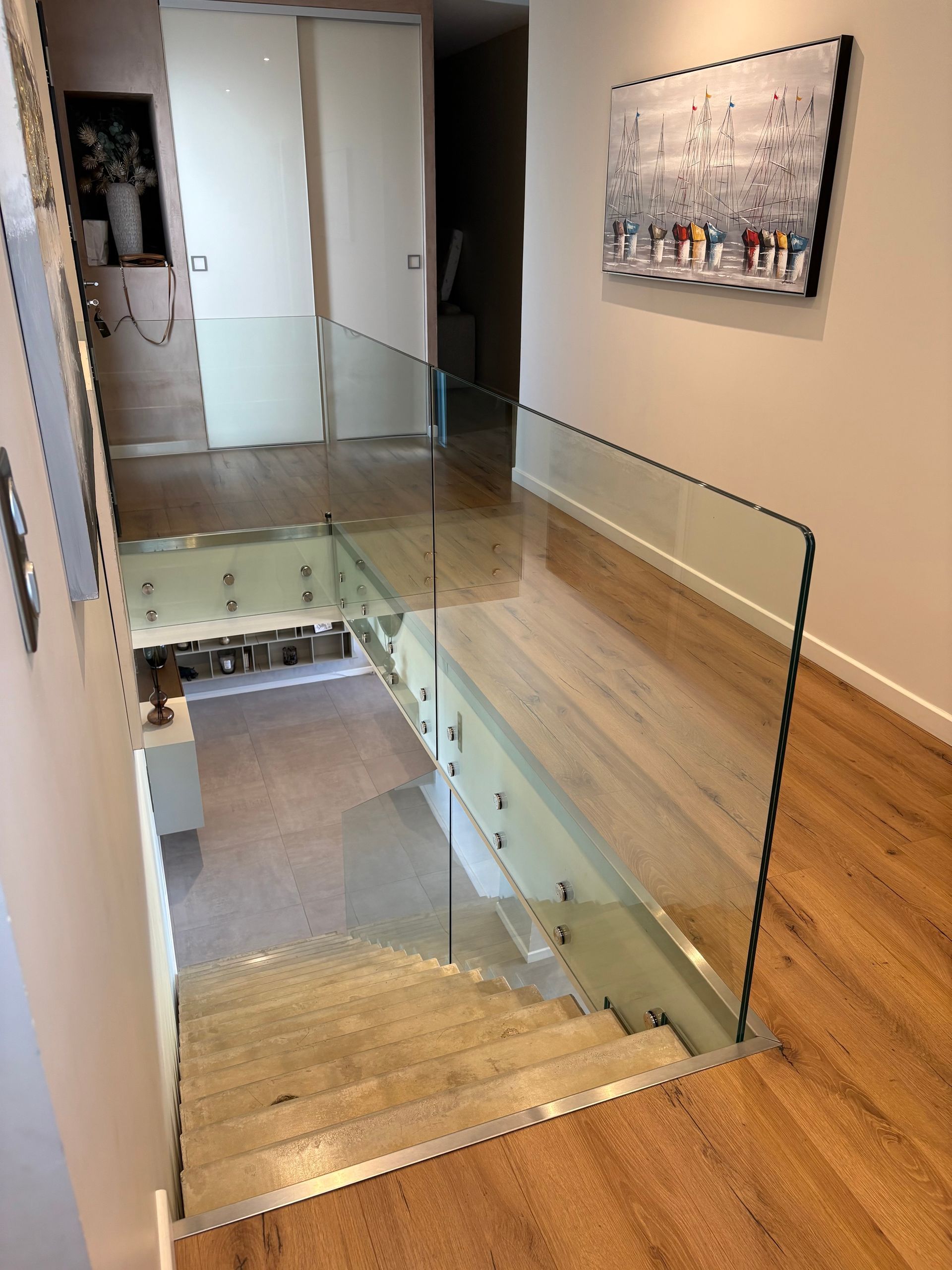 Une balustrade en verre surplombe un escalier aux marches en bois.