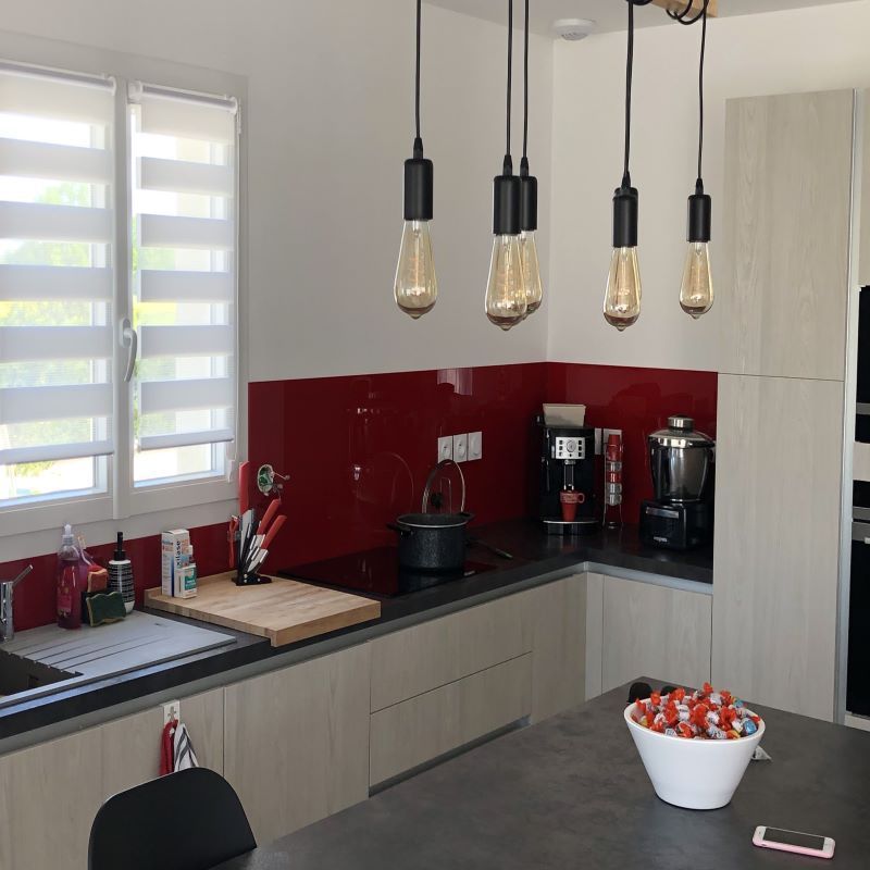 Cuisine moderne avec armoires en bois, crédence rouge vif, comptoirs noirs et quatre ampoules suspendues de style Edison.