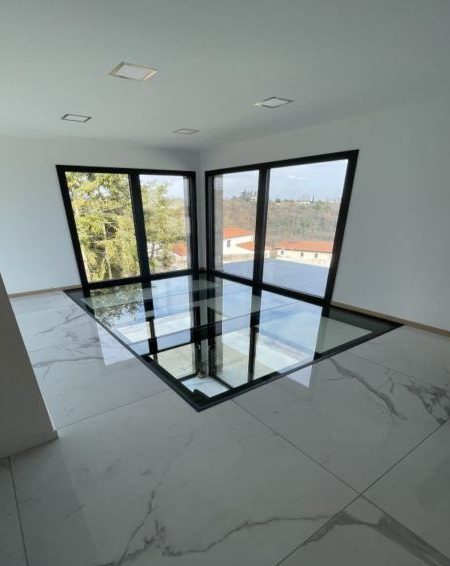 Une pièce avec un sol en marbre et un grand panneau de verre carré donnant sur un niveau inférieur.