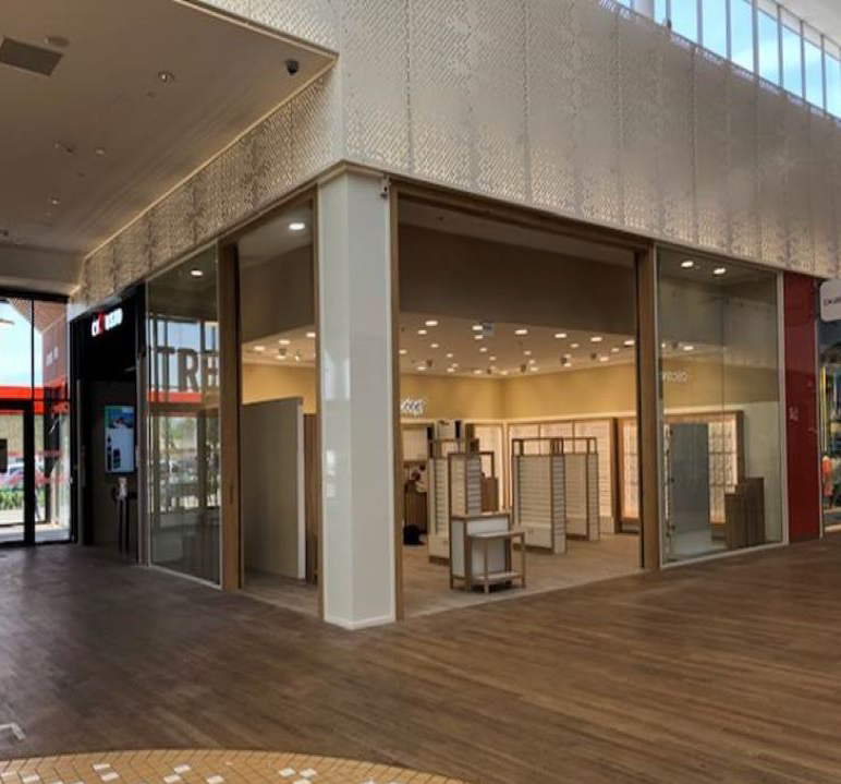 Une boutique d'angle aux parois vitrées du sol au plafond, dévoilant des étagères intérieures en bois clair.