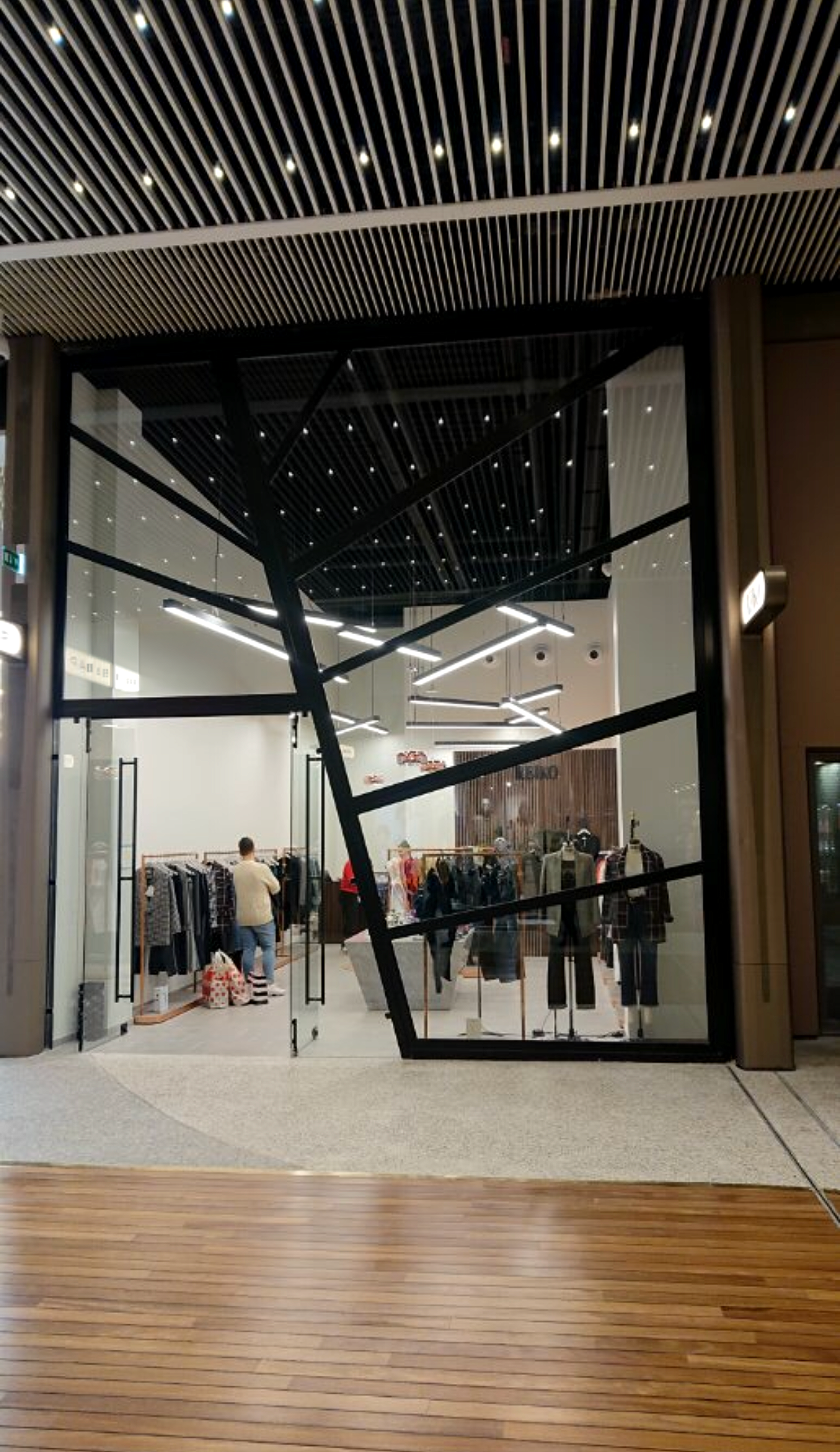 Vitrine vitrée d'un magasin de vêtements laissant apparaître des mannequins et des portants de vêtements.