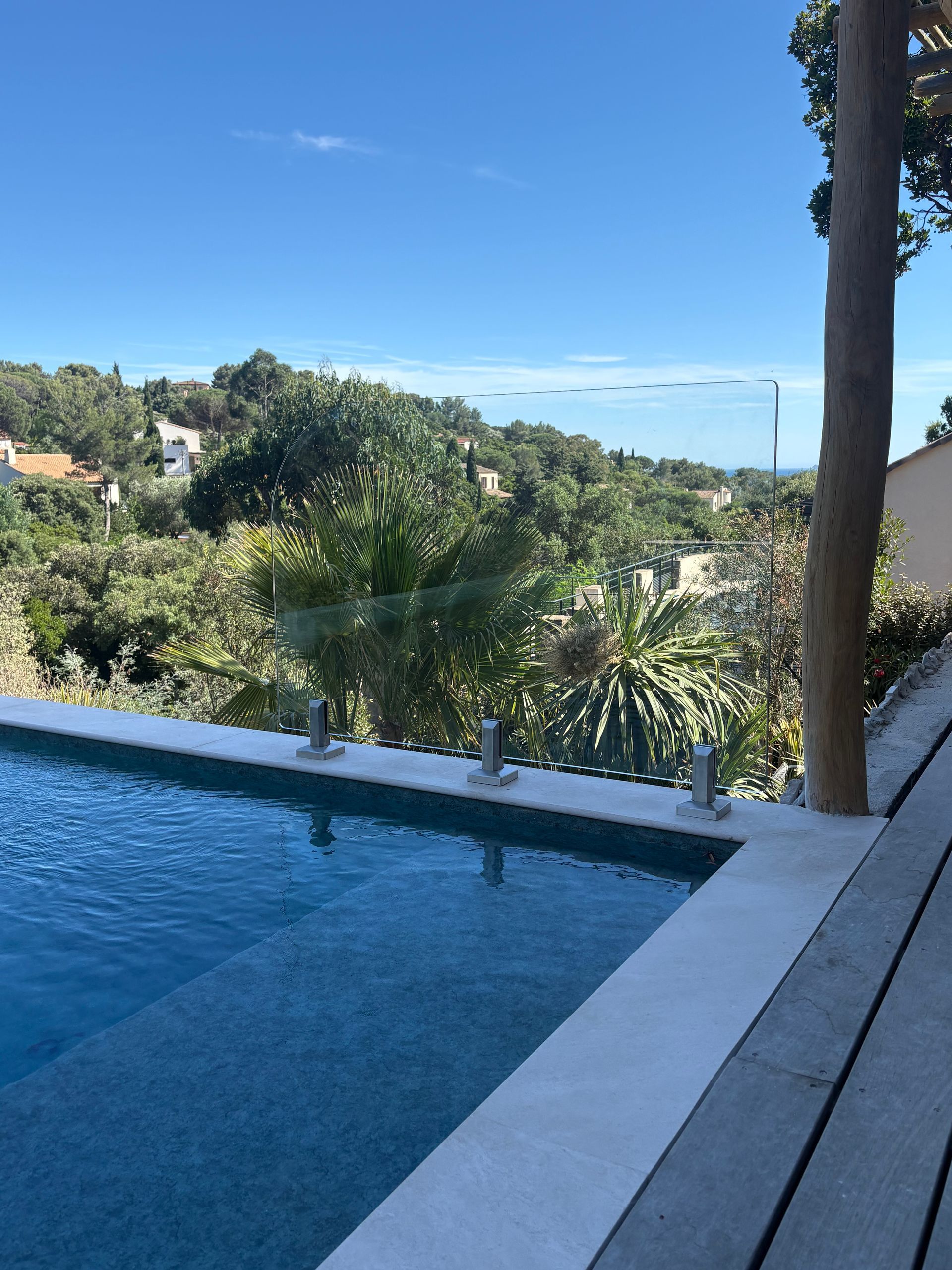Piscine à débordement surplombant une colline verdoyante sous un ciel bleu azur.