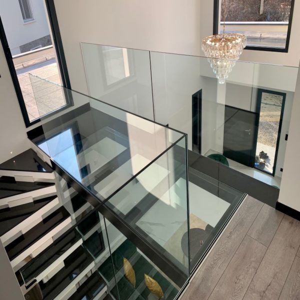 Intérieur d'une maison moderne : escalier en verre avec marches noires et blanches, rampe en verre et lustre.