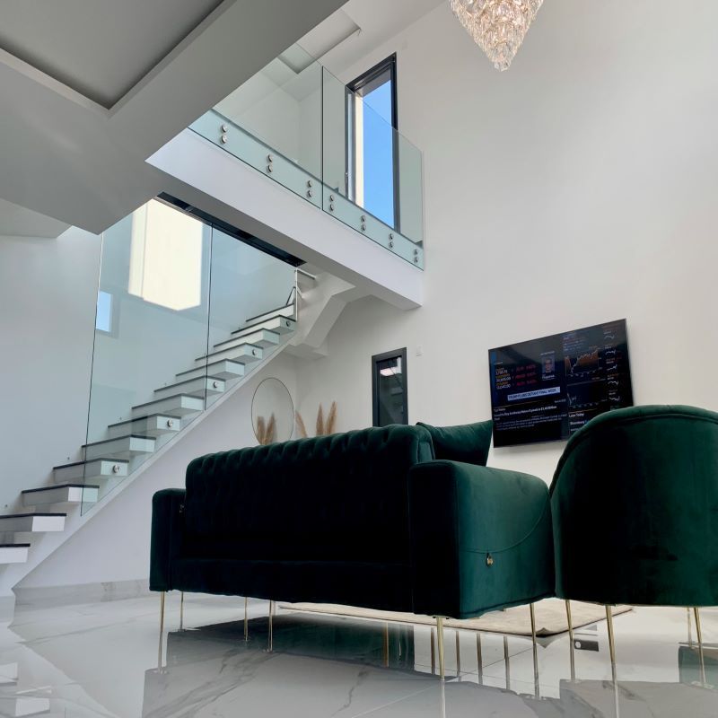 Salon moderne avec un canapé en velours vert, des murs blancs, un sol en marbre, un escalier suspendu et une télévision fixée au mur.