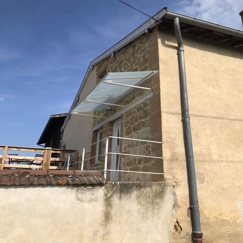 Vue latérale d'un bâtiment avec une verrière au-dessus de la porte, un mur en pierre et une balustrade métallique.