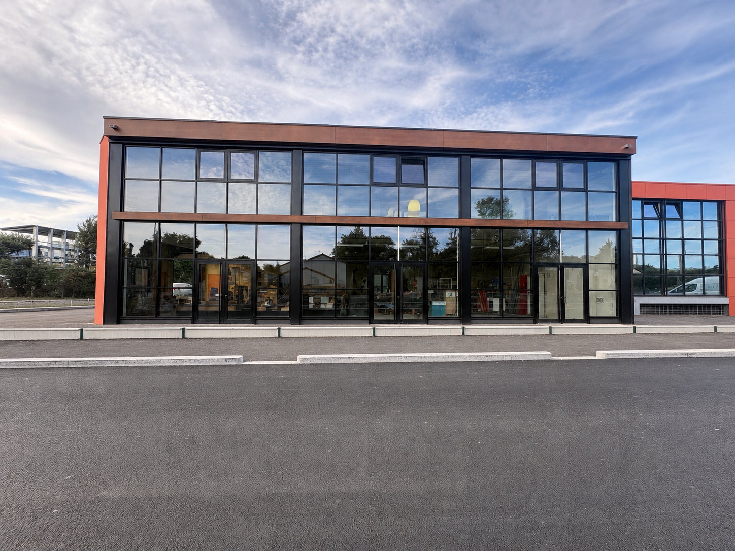 Immeuble commercial moderne à façade vitrée et finitions rouges, vu depuis une rue déserte.