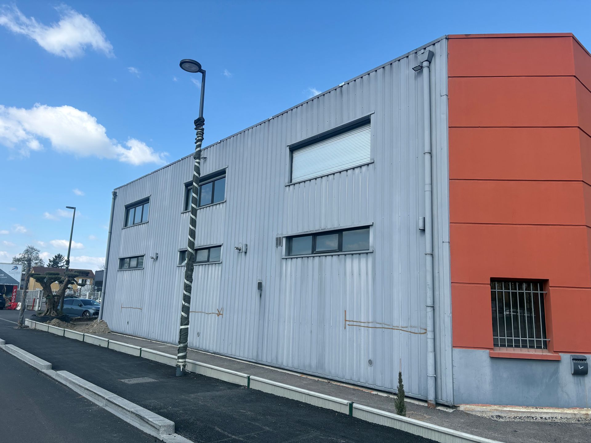 Bâtiment industriel blanc avec des panneaux d'angle orange en bord de route sous un ciel bleu