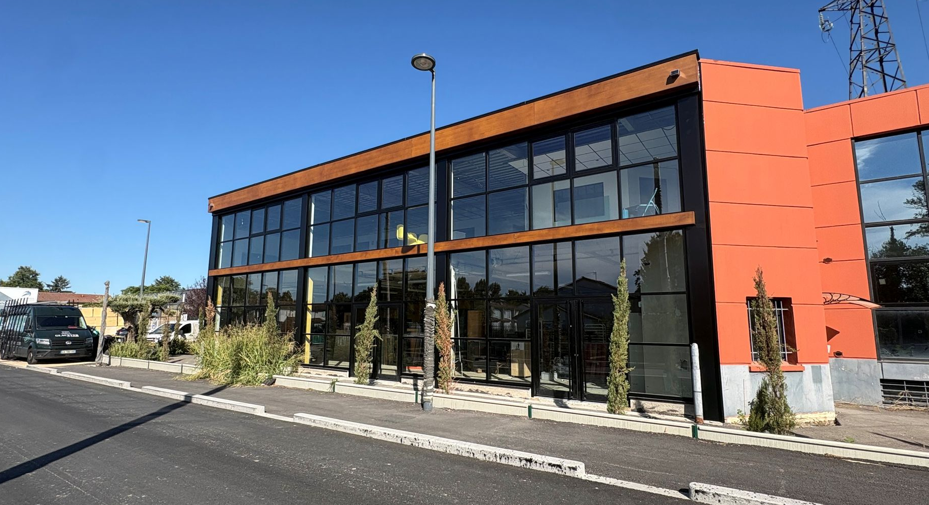 Immeuble de bureaux moderne de deux étages en verre avec des touches d'orange, situé en bordure de rue et de trottoir.