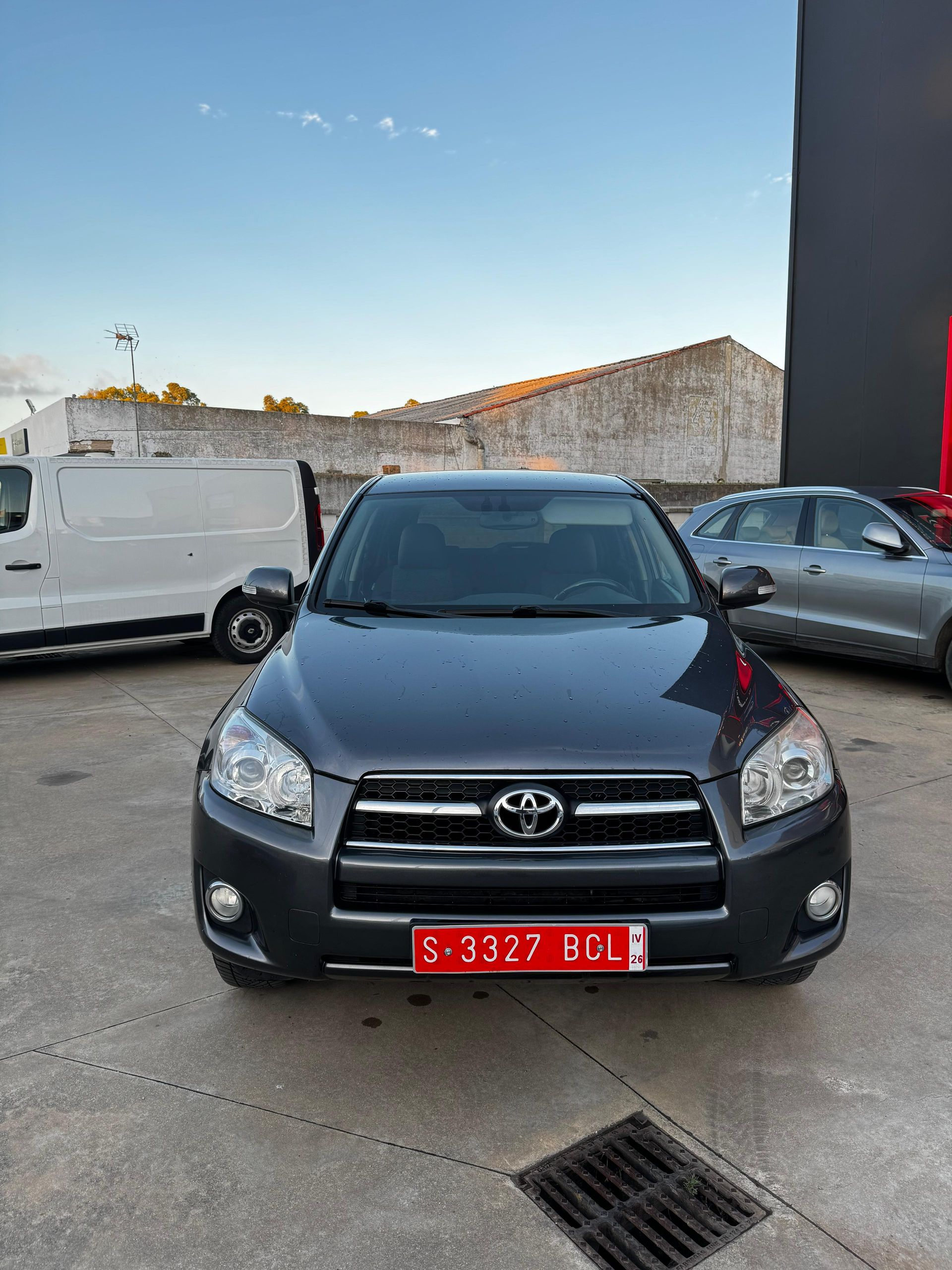 Un Toyota RAV4 gris oscuro con matrícula roja está aparcado afuera.