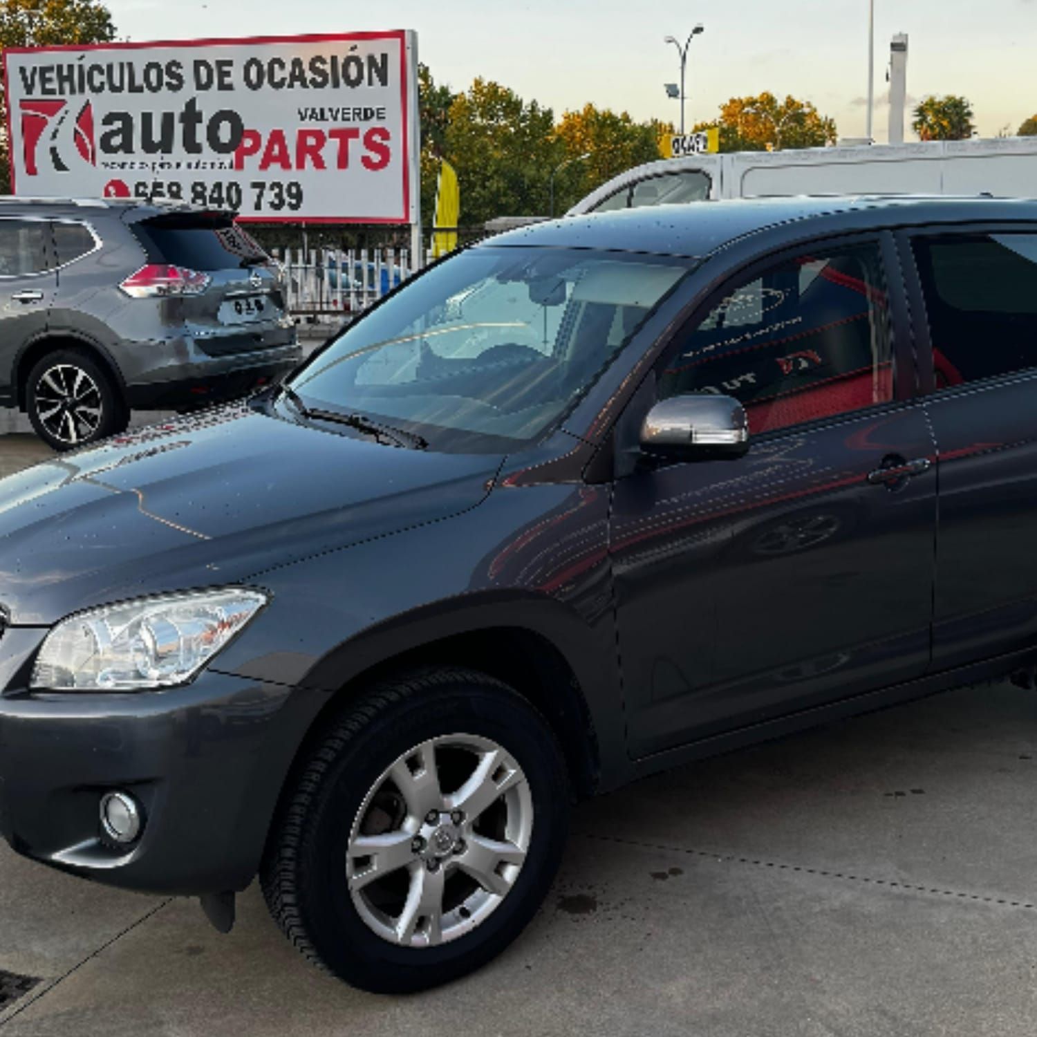 Un Toyota RAV4 gris oscuro estacionado frente a una tienda de repuestos para automóviles con un letrero.